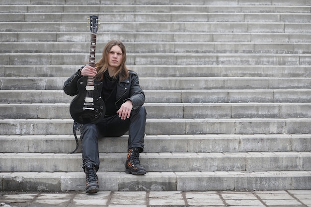 Rockgitarrist auf den stufen. ein musiker mit einer bassgitarre in einem lederanzug. metalist mit gitarre vor dem hintergrund des industrieschritts.