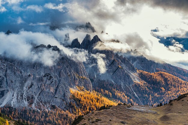 Rocky Mountains bedeckt mit Wolken und bunten Bäumen in der Herbstsaison, Dolomitenalpen, Italien