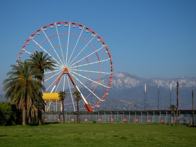 Roda-gigante contra o pano de fundo de montanhas e palmeiras Costa da cidade do sul Parque de diversões e montanhas