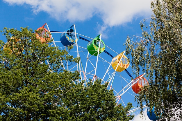 Roda-gigante de cores vivas no parque contra um céu azul com nuvens.