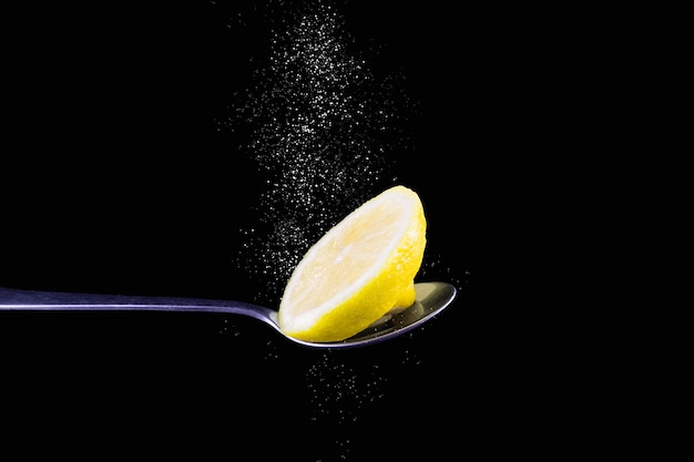 Rodaja de limón en una cuchara de metal con polvo blanco que gotea desde arriba sobre fondo negro