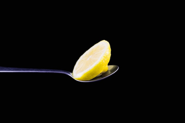 Rodaja de limón en una cuchara de metal sobre fondo negro