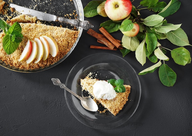 una rodaja de manzana crumble con helado en un plato de vidrio con una ramita de manzanas en el fondo