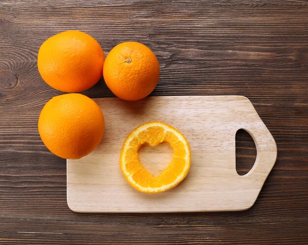 Rodaja de naranja con corte en forma de corazón y frutas sobre fondo de madera