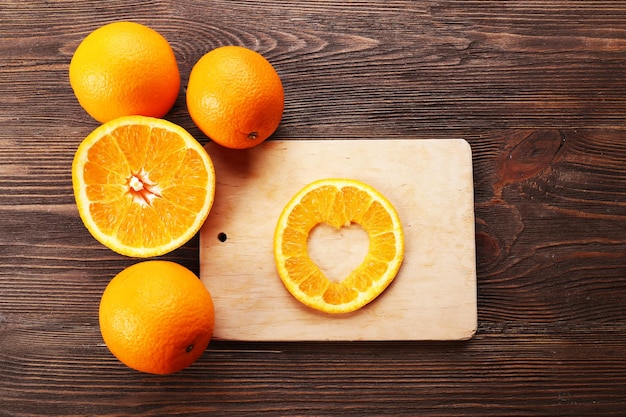 Rodaja de naranja con corte en forma de corazón y frutas sobre fondo de madera