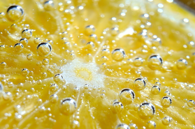 una rodaja de naranja cubierta de burbujas se encuentra en un vaso de agua con gas. De cerca.