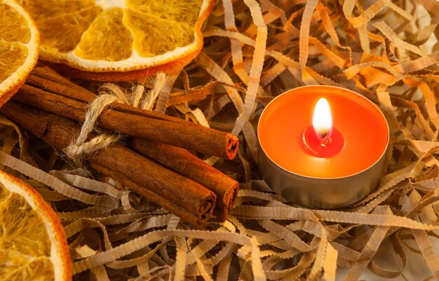 Rodaja de naranja y fragantes palitos de canela con una vela roja encendida