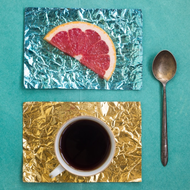 Rodaja de naranja y una taza de café en soportes hechos de lámina de color amarillo y turquesa sobre una superficie de madera