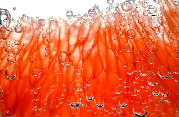 Foto rodaja de pomelo cápsulas pulposas peladas en agua con burbujas de aire en la luz de fondo primer plano enfoque selectivo