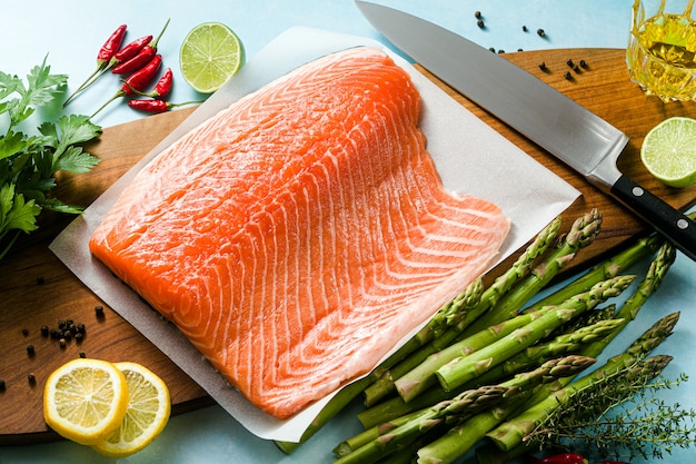 Rodaja de salmón fresco en una tabla de cortar de madera con hierbas aromáticas frescas y espárragos sobre la mesa. Receta de cocina. Fondo de alimentos. productos de pescado fresco