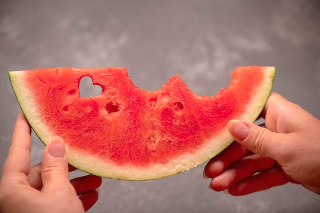 Una rodaja de sandía en las manos con un agujero en forma de corazón.