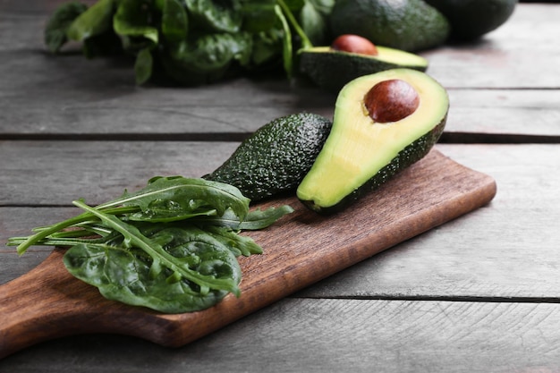 Rodajas de aguacate con espinacas y rúcula sobre tabla de cortar de madera