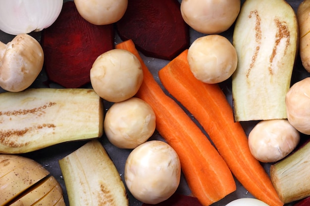 Rodajas de berenjena, remolacha, zanahorias, cebollas, patatas y champiñones enteros sobre papel pergamino antes de hornear alimentos saludables closeup