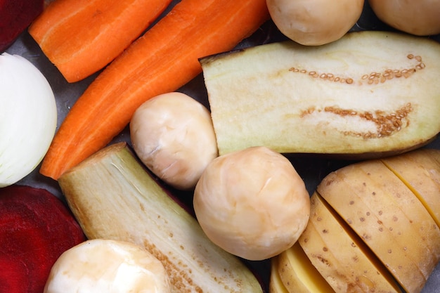 Rodajas de berenjena, remolacha, zanahorias, cebollas, patatas y champiñones enteros sobre papel pergamino antes de hornear alimentos saludables closeup