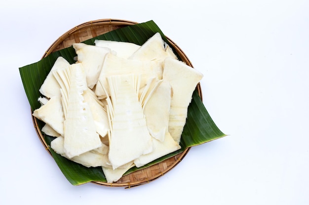 Rodajas de brotes de bambú crudo en cesta de bambú sobre fondo blanco.