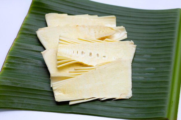 Rodajas de brotes de bambú crudo en hoja de plátano sobre fondo blanco.