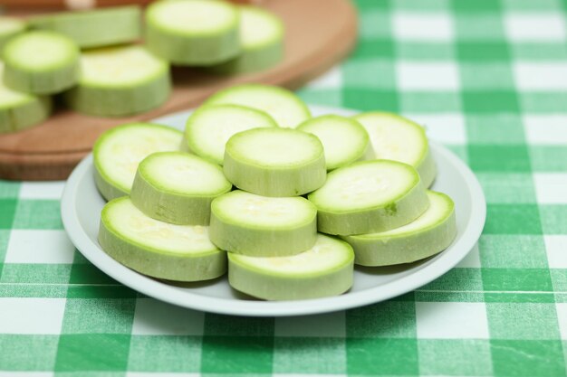 Rodajas de calabacín en un plato blanco y una tabla de madera sobre un mantel verde Verduras saludables Primer plano