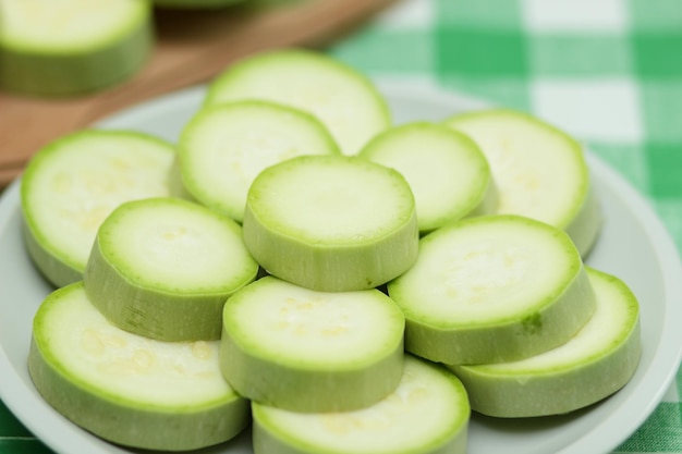 Foto rodajas de calabacín en un plato blanco y una tabla de madera sobre un mantel verde verduras saludables primer plano