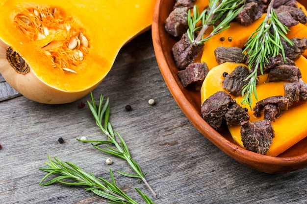 Rodajas de calabaza al horno con carne en una olla de barro. Comida otoñal con romero y especias