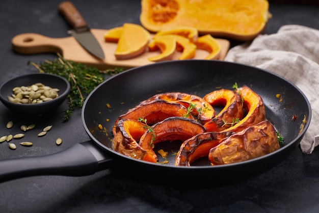 Rodajas de calabaza al horno en una sartén con tomillo y semillas comida vegetariana saludable en una mesa de piedra negra