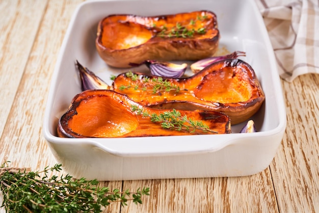 Rodajas de calabaza al horno y tomillo en una bandeja para hornear blanca de cerca