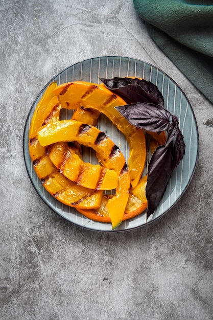 Rodajas de calabaza a la parrilla en un plato con hojas de albahaca en gris