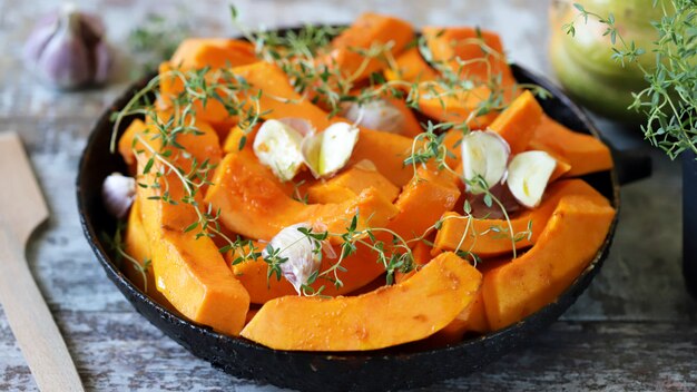 Rodajas de calabaza con tomillo y ajo en una sartén antes de hornear. Comida sana de otoño. Almuerzo vegano.