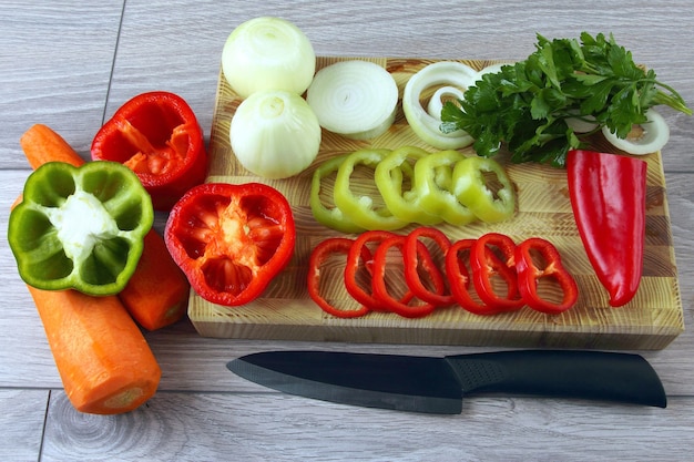 Rodajas de cebolla y pimiento sobre una tabla de cocina con perejil y zanahorias. Alimentos crudos. Ingredientes para cocinar