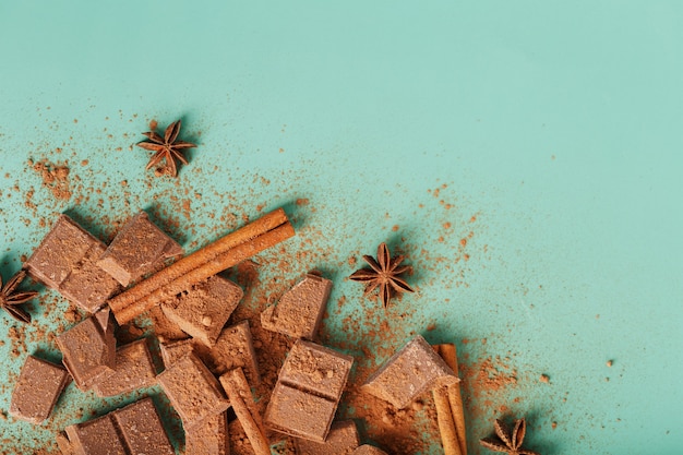 Rodajas de chocolate negro con canela y especias sobre una superficie verde pastel