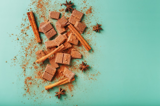 Rodajas de chocolate negro con canela y especias sobre una superficie verde pastel