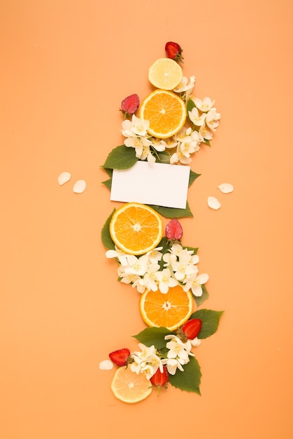 Rodajas de cítricos y fresas con flores de jazmín de jardín con hojas y tarjeta en blanco