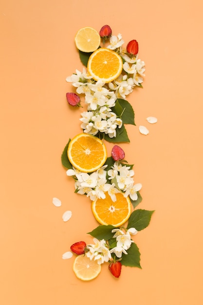 Rodajas de cítricos y fresas con flores de jazmín de jardín sobre un fondo naranja Fondo de verano