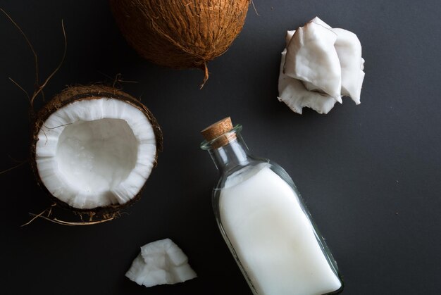 rodajas de coco fresco con una botella de aceite de coco prensado en frío sobre un fondo negro