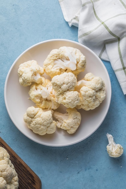 Foto rodajas de coliflor cruda en un recipiente ligero sobre un fondo azul con espacio de copia.