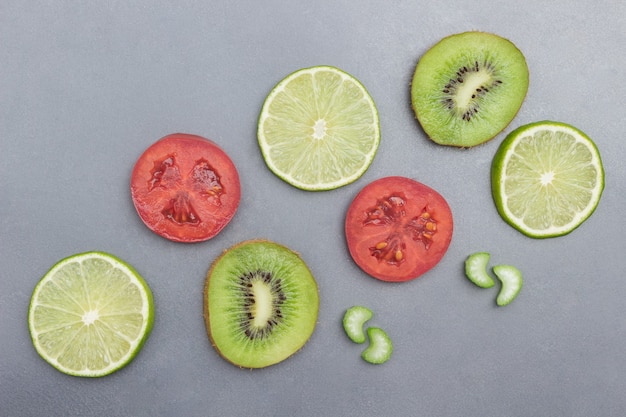 Rodajas de fruta de kiwi, lima y tomate sobre superficie gris