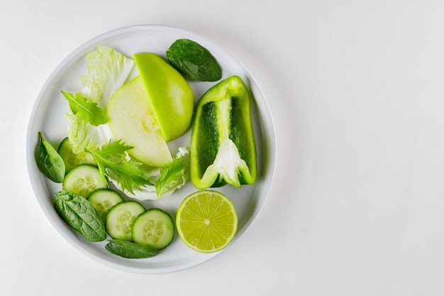 Rodajas de frutas y verduras en un plato blanco. Alimentos frescos de dieta verde sobre fondo blanco. Concepto de comida vegetariana saludable. Copie el espacio. Vista superior