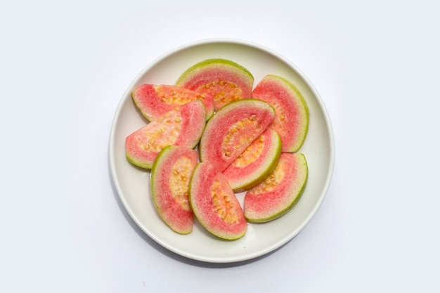 Rodajas de guayaba rosa fresca en plato blanco sobre fondo blanco.