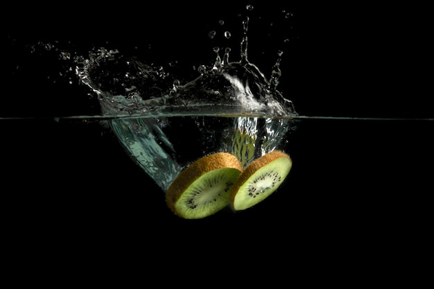 Rodajas de kiwi caen al agua y el agua salpica.