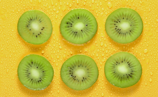 Rodajas de kiwi en gotas de agua sobre un fondo amarillo. Concepto de fruta.