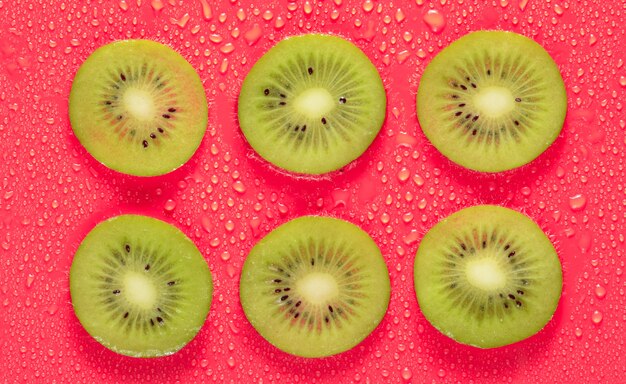 Rodajas de kiwi en gotas de agua sobre un fondo rojo. Concepto de fruta.