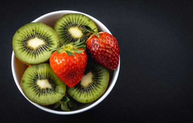Rodajas de kiwis y fresas en un tazón blanco sobre negro