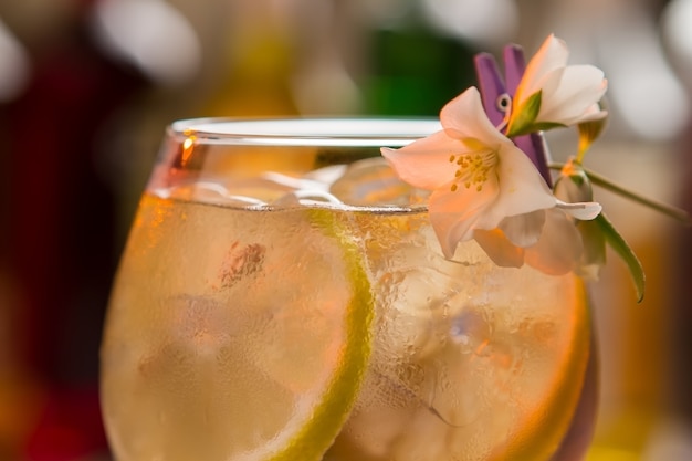 Rodajas de limón en bebida. Copa de vino decorada con flor de jazmín. Tom collins fresco con ginebra. Agua y jugo carbonatados.