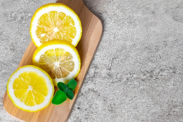 Rodajas de limón con hojas de menta para el tratamiento de la enfermedad en una tabla de cortar de madera sobre una mesa de piedra.