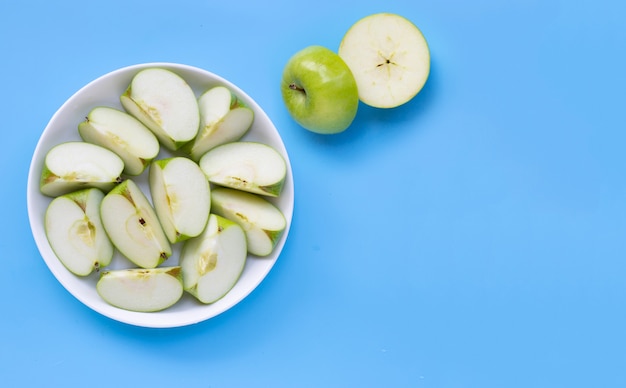 Rodajas de manzana verde fresca en un plato blanco sobre fondo azul.