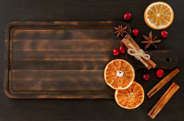 Rodajas de naranja, arándanos, canela y anís sobre una tabla de cortar oscura.