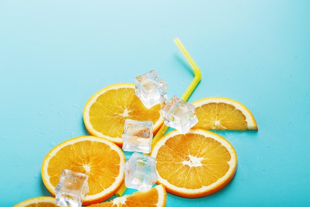 Rodajas de naranja y cubitos de hielo con una pajita sobre un azul