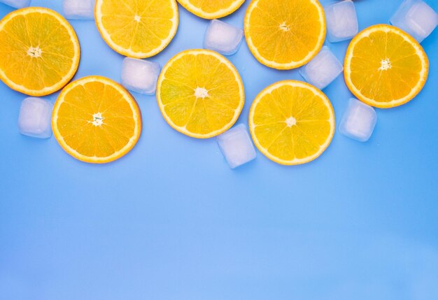 Rodajas de naranja y cubitos de hielo sobre un fondo azul.