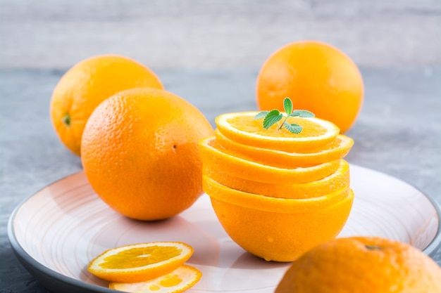 Rodajas de naranja fresca en una pila y hojas de menta en un plato sobre la mesa