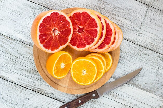 Foto rodajas de naranja y limón sobre una tabla de madera y un cuchillo.