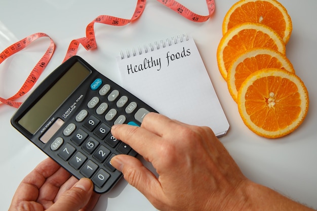 Foto rodajas de naranja, una nota en blanco y una cinta métrica. calorías contando con una calculadora. concepto de dieta